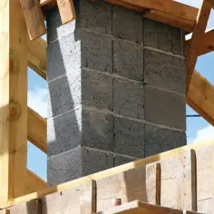 Budowa komina systemowego z bloczków betonowych, widoczny fundament i drewniana konstrukcja dachu.