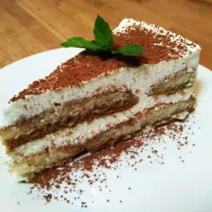 Pyszny kawałek najprostszego tiramisu, posypany kakao i udekorowany listkiem mięty.