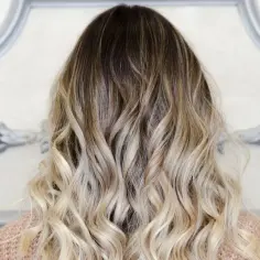 Włosy z efektem ombre blond, falowane, z ciemniejszymi końcówkami przechodzącymi w jasny blond.