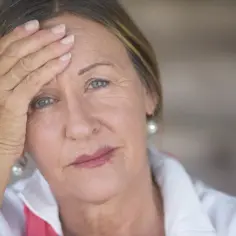 Zmartwiona kobieta z ręką na czole, szukająca ulgi w objawach menopauzy.
