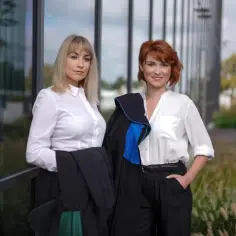 Dwie kobiety w togach prawniczych stoją przed nowoczesnym budynkiem.