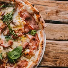 Pizza Carbonara z bekonem, rukolą i cebulą na drewnianym tle.