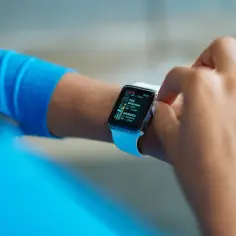 Osoba w niebieskiej bluzie sprawdza na smartwatchu listę kawiarni. Zastanawiasz się, jaka jest różnica między smartwatchem a opaską sportową i co kupić?