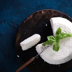 Świeży biały ser, doskonały jako alternatywa dla sera pecorino, z listkiem bazylii na drewnianej desce.