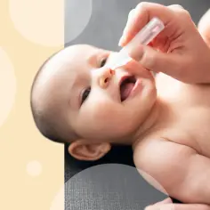 Mama zakrapla kropelki do noska, by ulżyć niemowlakowi z zatkanym nosem. Dziecko patrzy z zaciekawieniem.