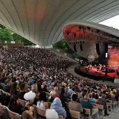 Koncert w jednym z polskich amfiteatrów. Tłum widzów siedzi na widowni, podziwiając występ zespołu na oświetlonej scenie.