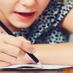 Dziecko zmagające się z pisaniem, być może objawy dysleksji. Skupiona twarz, ręka trzymająca ołówek nad zeszytem.