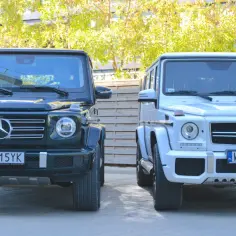 Dwa luksusowe mercedesy jeep stoją obok siebie. Jeden jest ciemnozielony, drugi biały.
