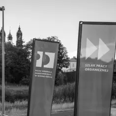 Dwie flagi informują o Szlaku Pracy Organicznej. Na jednej logo i nazwa Pałacu Generała Dąbrowskiego.