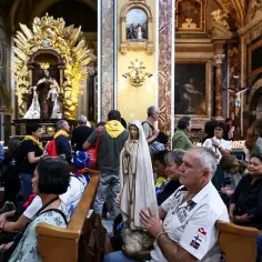 Ludzie w kościele, wśród nich mężczyzna niosący figurę Matki Bożej, świadczą o najnowszych objawieniach maryjnych na świecie.