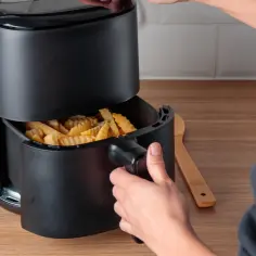 Ręka wyjmuje koszyk z frytkami z frytkownicy beztłuszczowej. To pokazuje, jak działa air fryer co to jest.