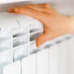 Dłoń dotyka białego grzejnika, sugerując kontrolę temperatury.