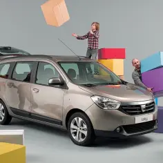 Rodzina pakuje rzeczy do Dacia Lodgy. Dzieci rzucają kartonami, a rodzice pomagają ładować bagaże.