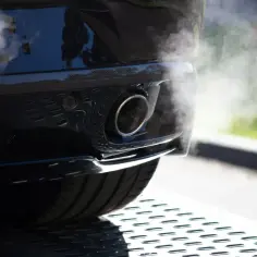 Dym wydobywa się z rury wydechowej samochodu, sugerując proces jak wypalić dpf na postoju.