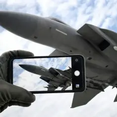 Ręka w rękawicy pilota trzyma smartfon, na którym widać myśliwiec. To jakby zapowiedź **Top Gun 3** – uchwycone w kadrze marzenie o przestworzach.