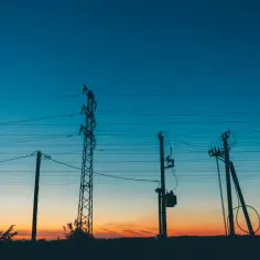 Sylwetki słupów energetycznych i transformatora na tle zachodzącego słońca. Czy należy się odszkodowanie za transformator na działce?