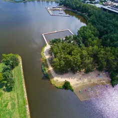 Widok z lotu ptaka na żwirownię z kąpieliskiem, plażą i lasem.