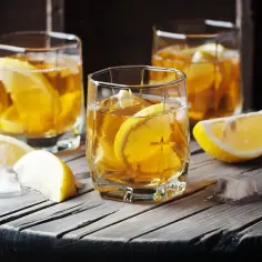 Trzy szklanki z bursztynowym napojem i plasterkami cytryny, idealne na orzeźwiające martini bianco.
