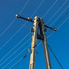 Słup energetyczny z przewodami na tle błękitnego nieba. Zastanawiasz się, ile wynosi odszkodowanie za słupy energetyczne na działce?