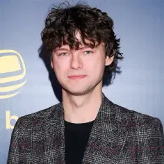 Mateusz Kościukiewicz, znany z wielu świetnych mateusz kościukiewicz filmów, na tle niebieskiej ścianki z logo.