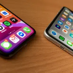 Dwa iPhone'y na drewnianym stole. Jeden z nich ma ikony aplikacji, jakby po udanym jailbreaku, z powiadomieniami.