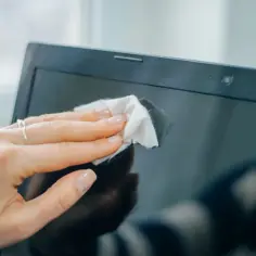Dłoń z delikatnym pierścionkiem czyści ekran laptopa, pokazując jak umyć monitor bez smug.