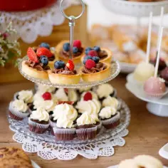 Słodkie przekąski: babeczki, tartaletki z owocami, cake pops i ciasto czekoladowe na drewnianym stole.