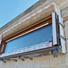 Ciepły montaż okien w trakcie budowy. Widoczny drewniany parapet, izolacja i system mocowania okna do ściany z bloczków.
