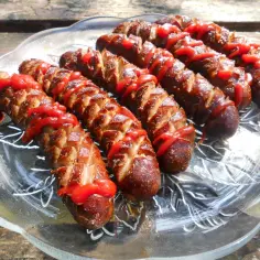 Kiełbasa z grilla inaczej: nacięta i polana ketchupem, ułożona na szklanej paterze. Idealna na letnie popołudnie.
