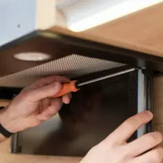 Ręce przykręcają element okapu kuchennego. Dowiedz się, jak podłączyć okap kuchenny bez komina, by cieszyć się czystym powietrzem.