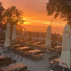Zachód słońca nad morzem, z pustymi stolikami i ławkami w ogródku restauracji na klifie. Idealne miejsce na rybę i mięso po dniu pełnym wrażeń.