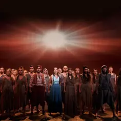 Aktorzy w teatrze roma w strojach ludowych, na tle dramatycznego, pomarańczowego nieba.