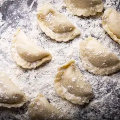 Surowe pierogi leżą na blacie oprószonym mąką. Jaki typ mąki na pierogi? Ta wygląda na pszenną, idealną do domowych wypieków.