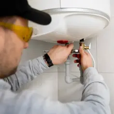 Instalator w okularach ochronnych podłącza bojler elektryczny.