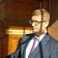 Prezydent Częstochowy w okularach, w garniturze, przy drzwiach sali rozpraw.