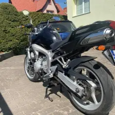 Czarny motocykl Yamaha FZ6 na podjeździe z kostki brukowej, w tle dom i zielone krzewy.