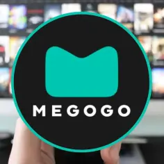 Ręka trzymająca pilot przed ekranem telewizora z logo Megogo. Sprawdź megogo opinie przed wyborem.