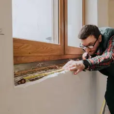 Mężczyzna mierzy parapet, planując, czym obrobić okna wewnątrz.