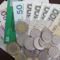 Pieniądze i monety na tle legitymacji emeryta. Ile wynosi 13 emerytura? ZUS wypłaci świadczenie.