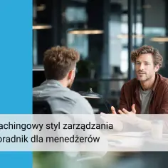 Dwóch mężczyzn rozmawia w biurze. Jeden z nich, w brązowej koszuli, gestykuluje, wyjaśniając coś. To przykład coachingowego stylu zarządzania.