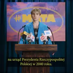 Młody mężczyzna w niebieskiej marynarce przemawia za mównicą z mikrofonami.
