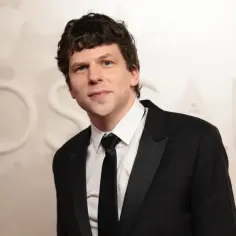 Jesse Eisenberg w czarnym smokingu z czarnym krawatem, na tle napisu OSCARS.