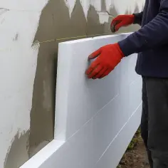 Pracownik w czerwonych rękawicach montuje styropian na ścianie. Określenie elewacja cena za m2 robocizna.