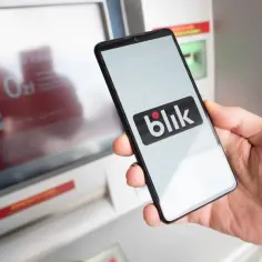 Dłoń trzyma smartfon z logo Blik. Kto wymyślił Blik? To polski system płatności mobilnych, który zrewolucjonizował transakcje.