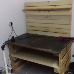 Solidny stół warsztatowy z palet, gotowy do pracy. Na blacie listwa zasilająca i małe urządzenie.