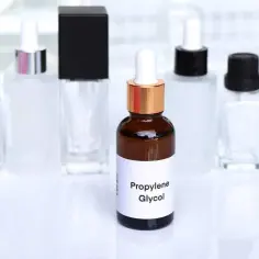 Butylene glycol w buteleczce z pipetką, otoczony innymi kosmetycznymi opakowaniami.