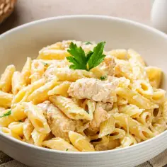 Makaron penne w kremowym sosie z kurczakiem, udekorowany natką pietruszki.