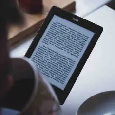 Osoba czyta książkę w formacie kindle. Na ekranie widoczny jest tekst powieści.