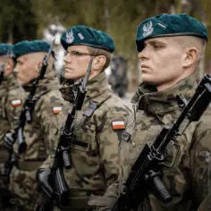 Żołnierze Wojska Polskiego w zielonych beretach i mundurach polowych, z karabinami w rękach, stoją w szeregu.