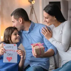 Wiersz o rodzinie: córka daje tacie kartkę "Happy Father's Day", mama obejmuje męża.